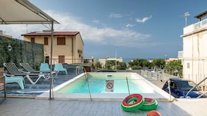 Una piscina en la azotea con sillones de descanso, un balón de baloncesto y flotadores.
