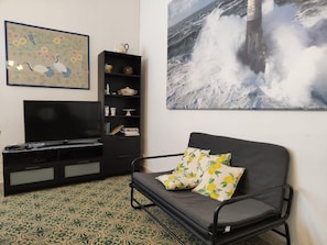 A living room with a sofa, a TV, a bookshelf, and a large painting of a wave crashing.