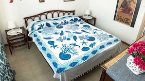 Un dormitorio con cama, dos mesitas de noche, una mesita auxiliar, un cartel en la pared y un jarrón con flores sobre una mesa.