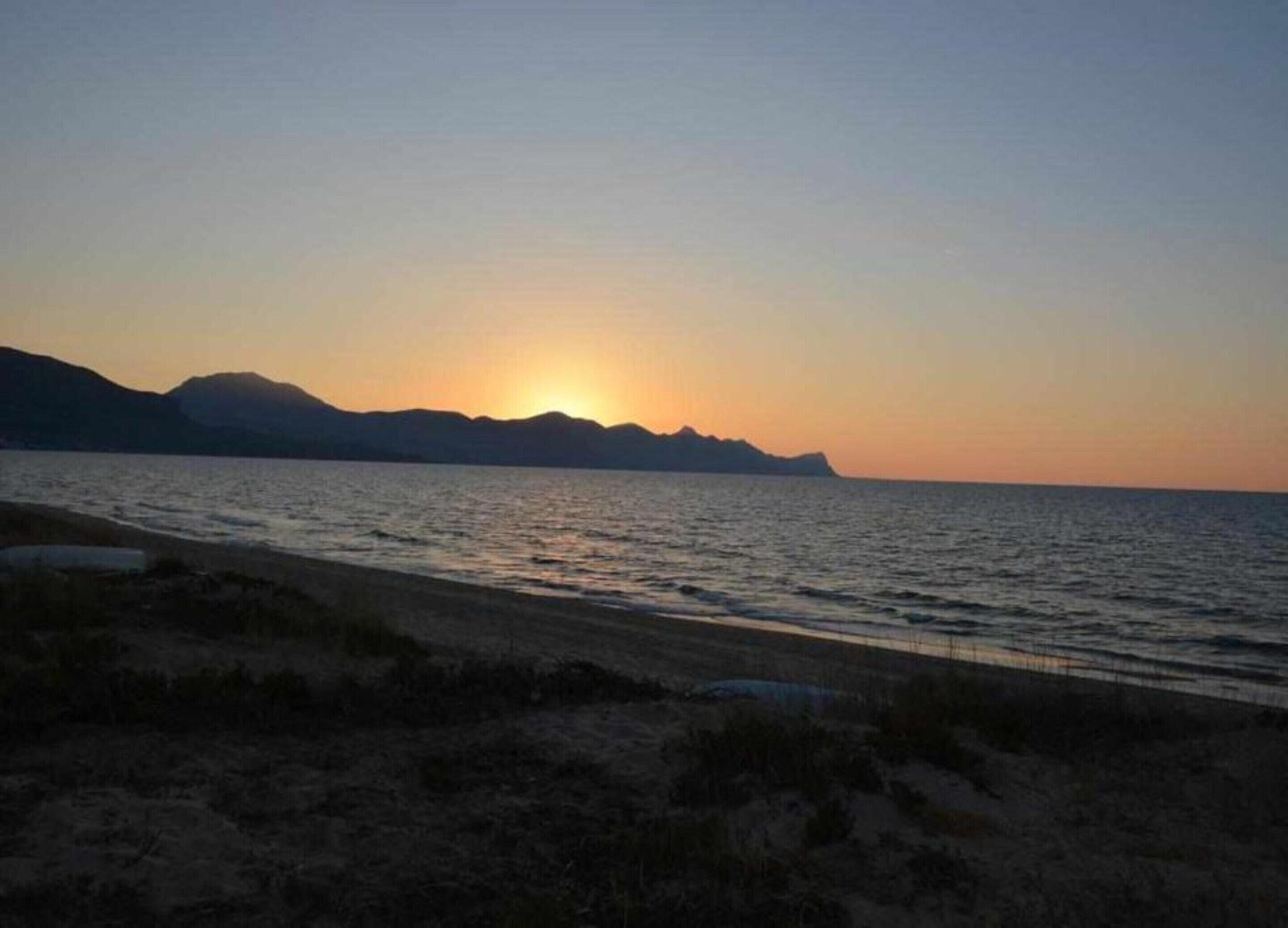 A beach with a sunset over the water and mountains in the background.