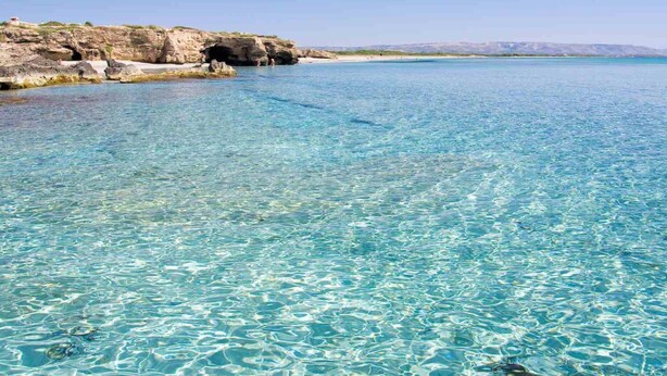 A coastal scene with clear turquoise water, rocky cliffs, and a distant shoreline. - Belvilla by OYO Acanto Bilocale (Modica)