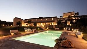 A pool area with lounge chairs and a stone building with multiple windows. - Belvilla by OYO Acanto Bilocale (Modica)