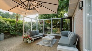 A covered patio with a white sofa, a small table, and potted plants.