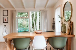 A dining area with a wooden table, two green chairs, and a white chair. There are framed pictures on the wall, a large mirror, and a vase with a plant. - Attractive Bungalow in Ouddorp With Garden (Ouddorp)