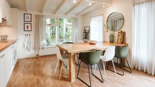 A dining area with a wooden table, four chairs, and a large mirror on the wall.