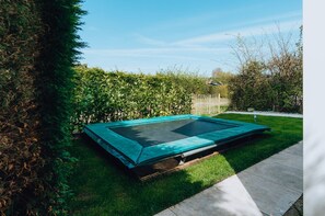 A trampoline in a backyard with a wooden deck and a hedge. - Large, Elegantly Furnished Holiday Home With Lots of Privacy on a Family Park (Ouddorp)