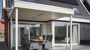 A covered patio with a table and chairs, a pumpkin on the table, and a view of the surrounding area. - Villa in Colijnsplaat by the Sea & Sauna (Colijnsplaat)