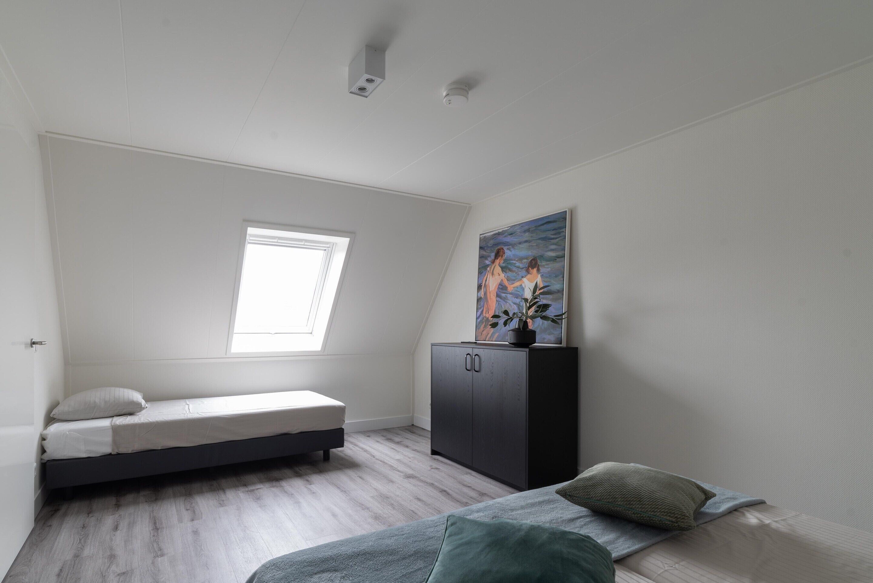 A small, modern bedroom with a loft bed, a window, a cabinet, and a painting.