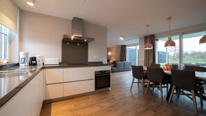 A modern kitchen with a central island, built-in oven, and stainless steel range hood. - Villa in Colijnsplaat by the Sea & Sauna (Colijnsplaat)
