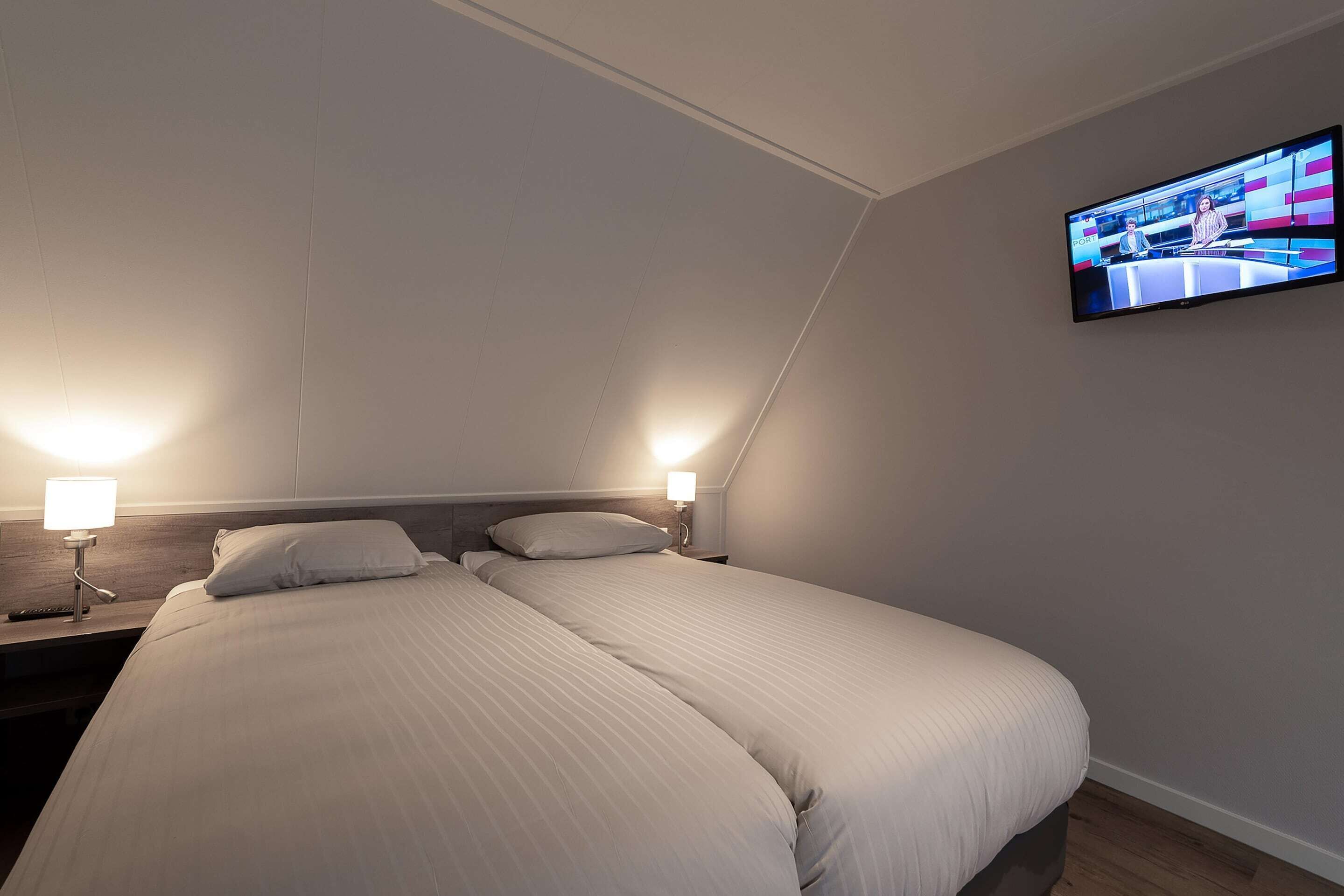 Une chambre d’hôtel avec un lit, deux lampes de chevet et un téléviseur fixé au mur.