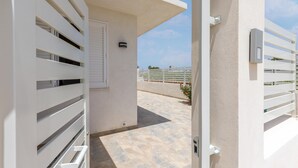 An open gate leading to a balcony with a tiled floor and a white fence in the background.