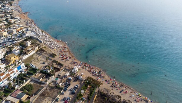 An aerial view of a coastal town with a beach, buildings, and parked cars.