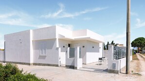 A modern white building with a flat roof, a small entrance with a door, and a paved driveway.
