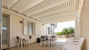 A covered patio area with a table and chairs, a window with shutters, and a view of the outside.