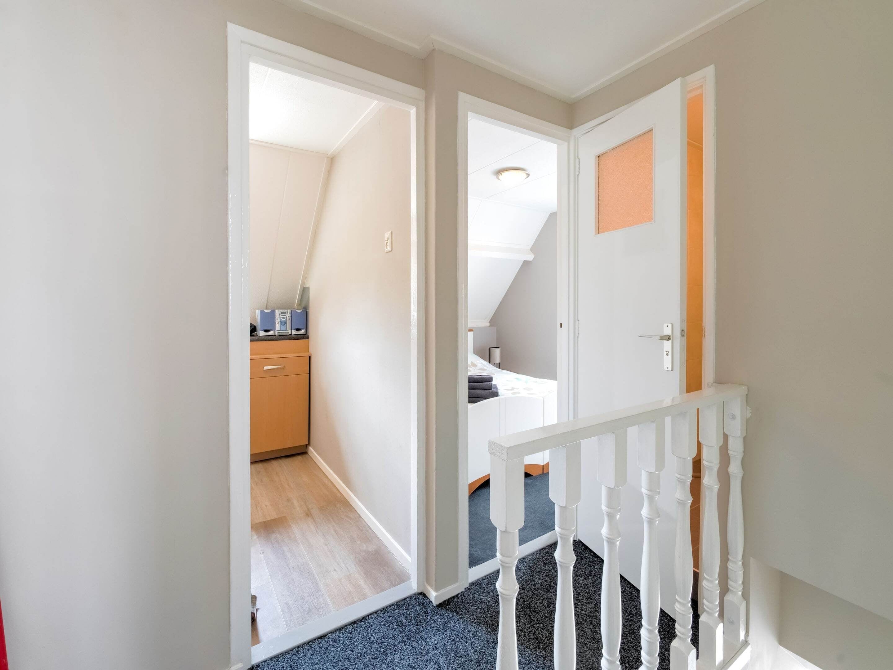 A hallway with a wooden floor, white walls, and a white railing.