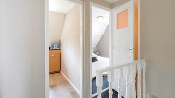 A hallway with a wooden floor, white walls, and a white railing.