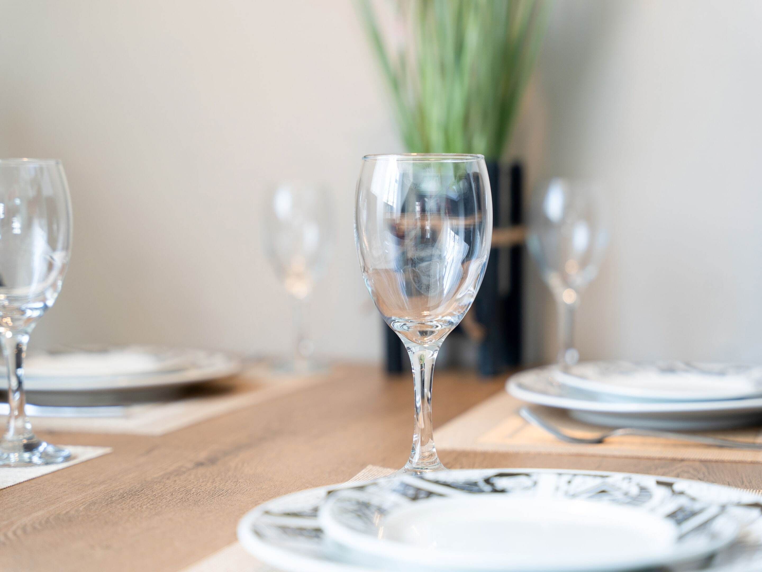 A dining table with a clear glass wine glass in the center, surrounded by plates and cutlery.