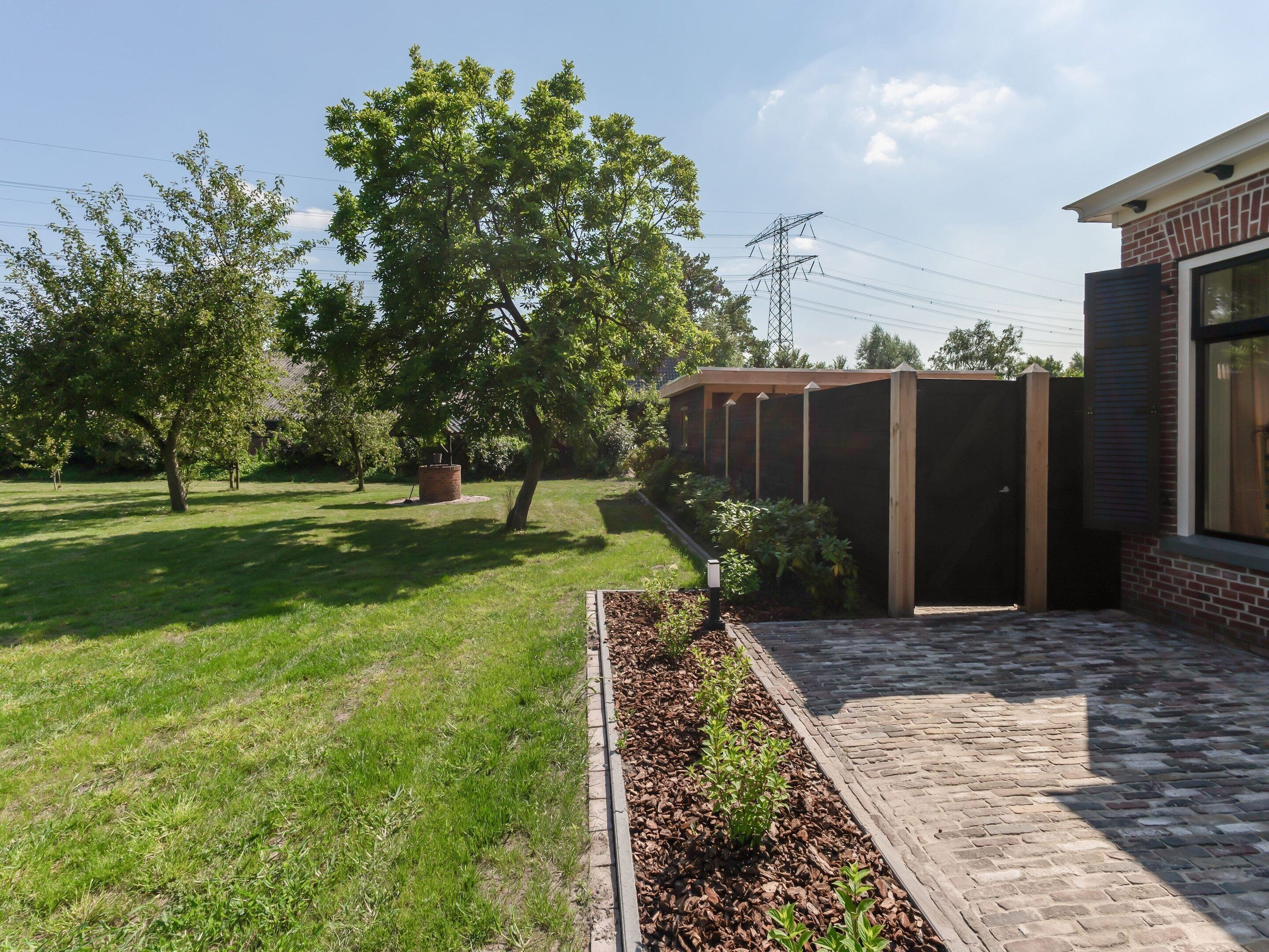 Ein Innenhof mit Pflasterweg, einer Holzpergola und einem großen Baum.