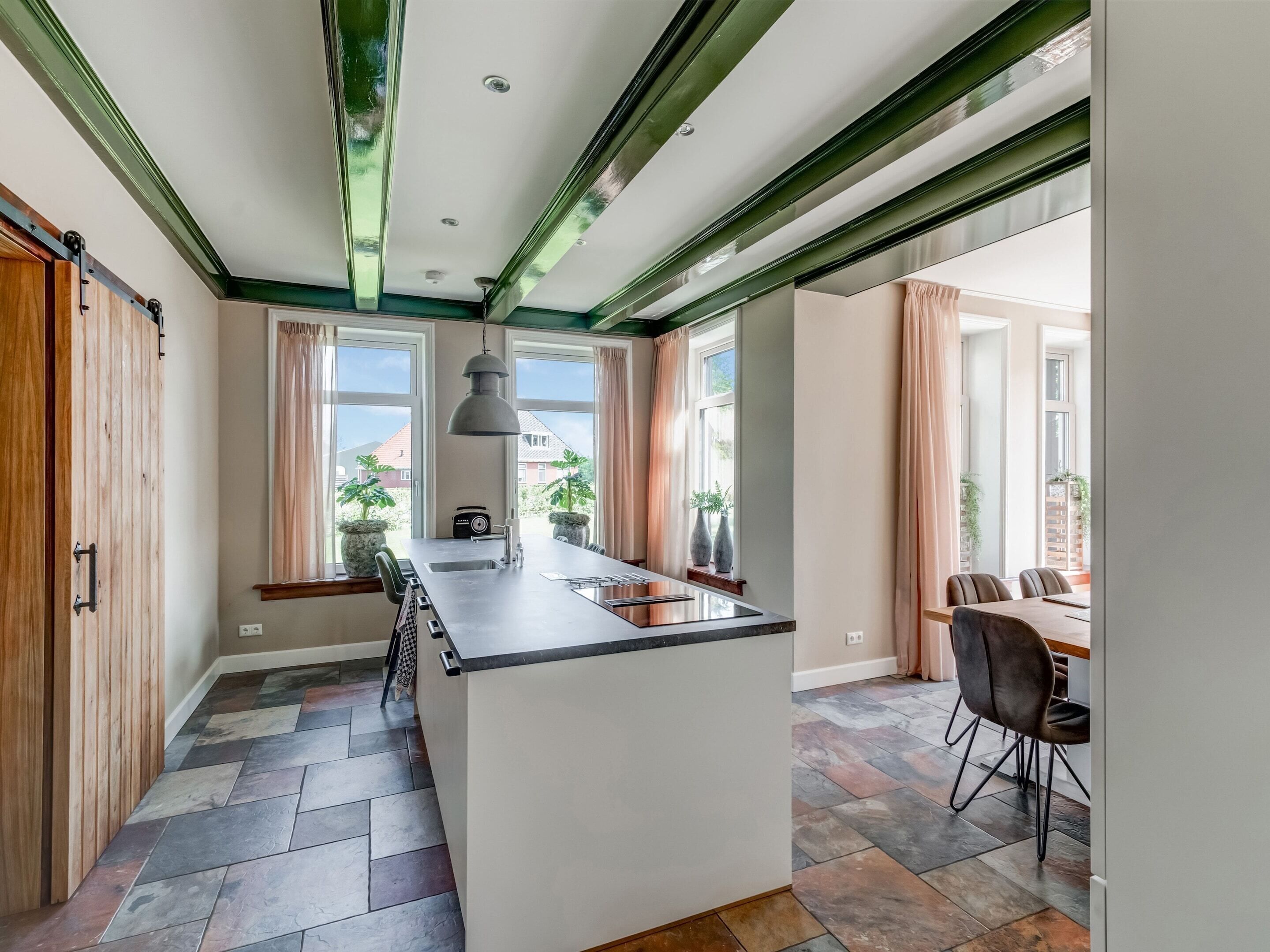 A modern kitchen with a central island, large windows, and a dining area with chairs.
