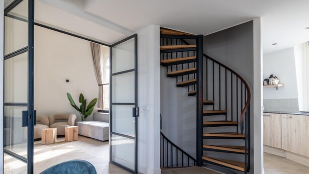 Een modern interieur met een spiltrap, een zithoek met een bank en salontafel, en een keukenhoek.