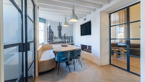 Een moderne keuken met een ingebouwde kookplaat, een eethoek met een houten tafel en blauwe stoelen, en een groot raam met uitzicht op de stad.