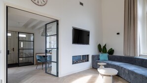 Een moderne woonkamer met een bank, een aan de muur bevestigde televisie en een open haard.