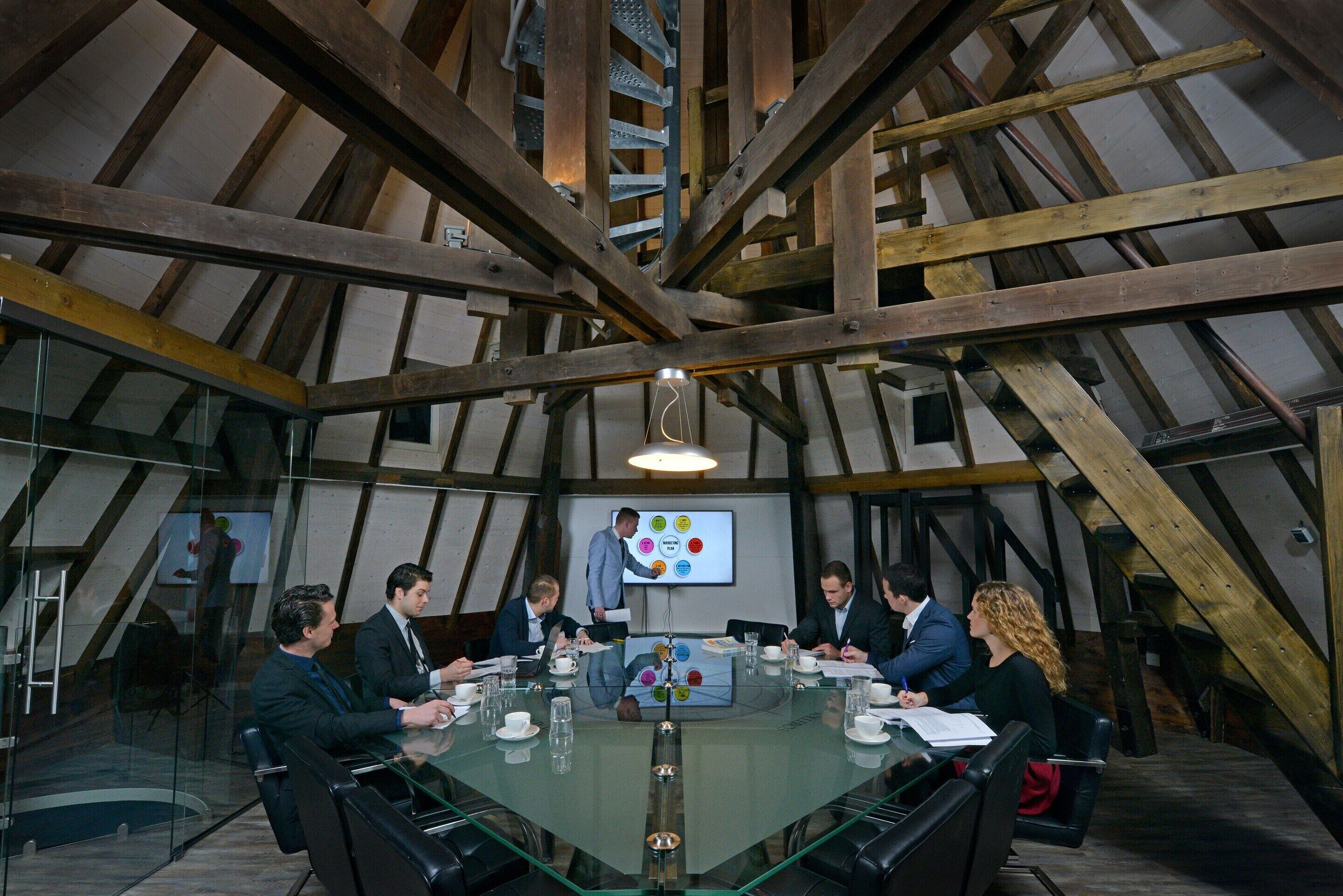 A conference room with a glass table, wooden beams, and a presentation screen.