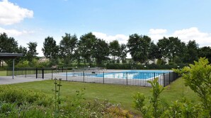 Una piscina rectangular envoltada per una tanca de metall negre, amb una zona enjardinada al primer pla i arbres al fons.