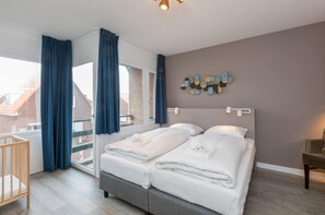 A bedroom with two beds, a crib, a balcony view, and a decorative wall piece. - Apartment in Zoutelande by the Beach (Zoutelande)