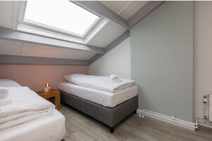 Una camera da letto con un lucernario, un letto con lenzuola bianche, un comodino con una lampada e un termosifone.