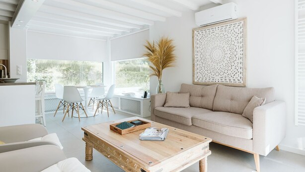 Ein modernes Wohnzimmer mit einem beigefarbenen Sofa, einem Holztisch und einem Essbereich mit weißem Tisch und Stühlen.