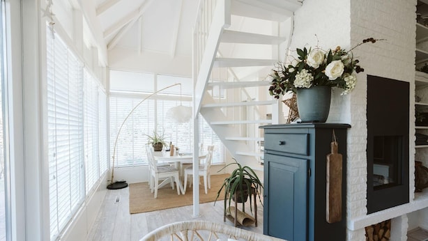 A bright, airy room with a white staircase, a dining area with a table and chairs, and a blue cabinet with a potted plant. - Lovely Holiday Home 10 Minutes by Bike (Ouddorp)