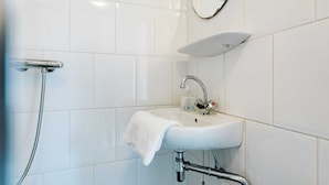 A bathroom with white tiles, a sink with a mirror above it, and a showerhead. - Village House, Authentic, Modern Living Room, Courtyard (Ouddorp)