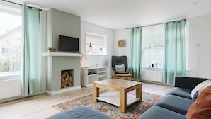 A living room with a sofa, a coffee table, a TV, a fireplace, and a window with curtains. - Village House, Authentic, Modern Living Room, Courtyard (Ouddorp)