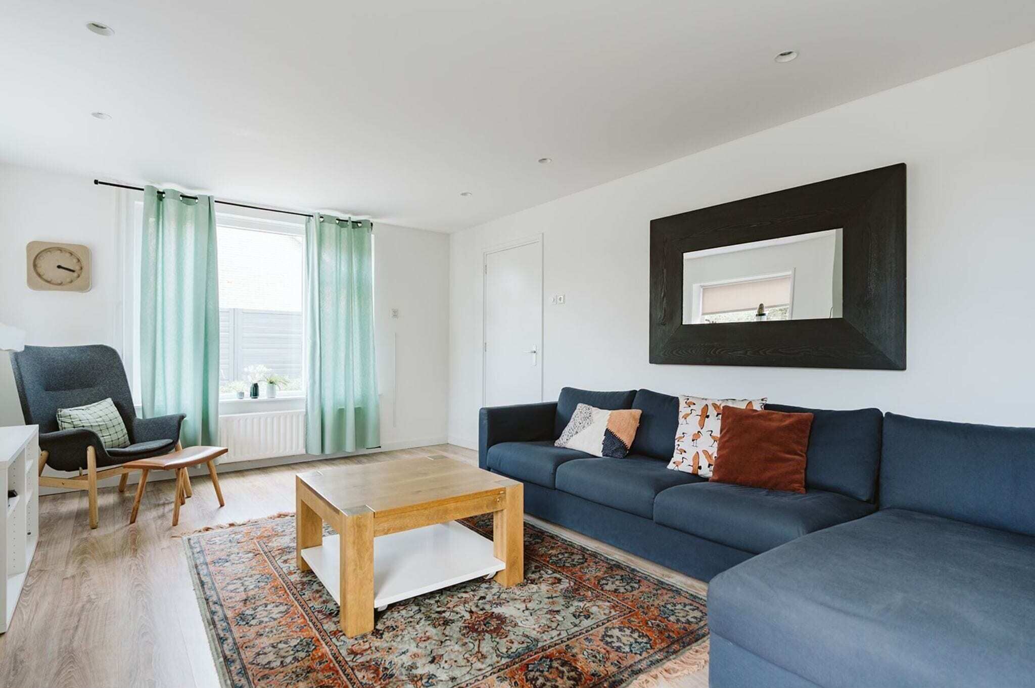 A modern living room with a blue sofa, a wooden coffee table, a patterned rug, and a large mirror on the wall.