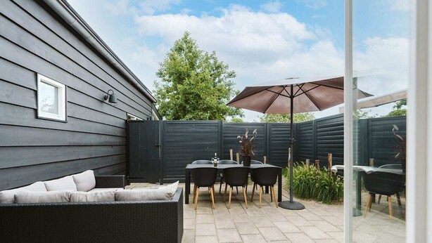 A patio with a black wicker sofa, a table with chairs, and a large umbrella. - Village House, Authentic, Modern Living Room, Courtyard (Ouddorp)