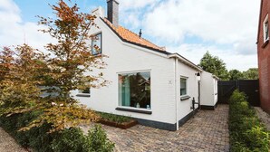 A white house with a tiled roof, a brick pathway, and a garden area. - Village House, Authentic, Modern Living Room, Courtyard (Ouddorp)