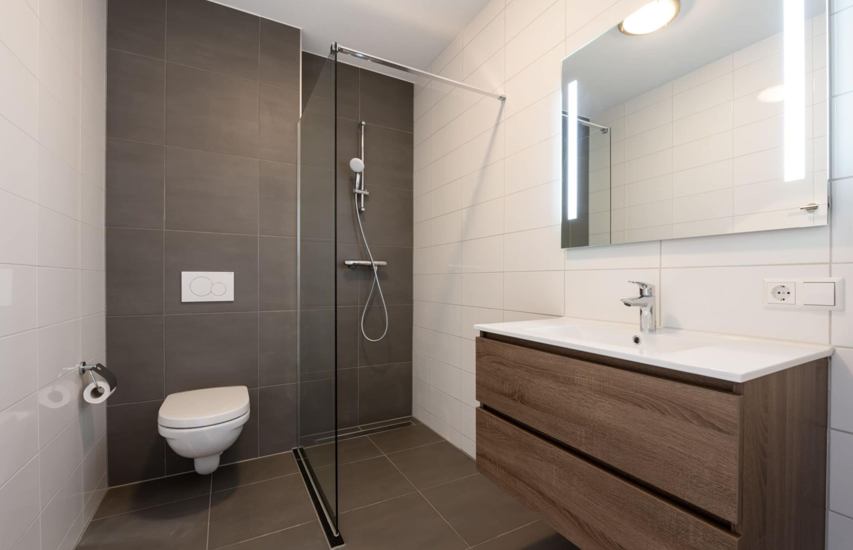 A modern bathroom with a glass-enclosed shower, a white toilet, and a wooden vanity with a mirror.