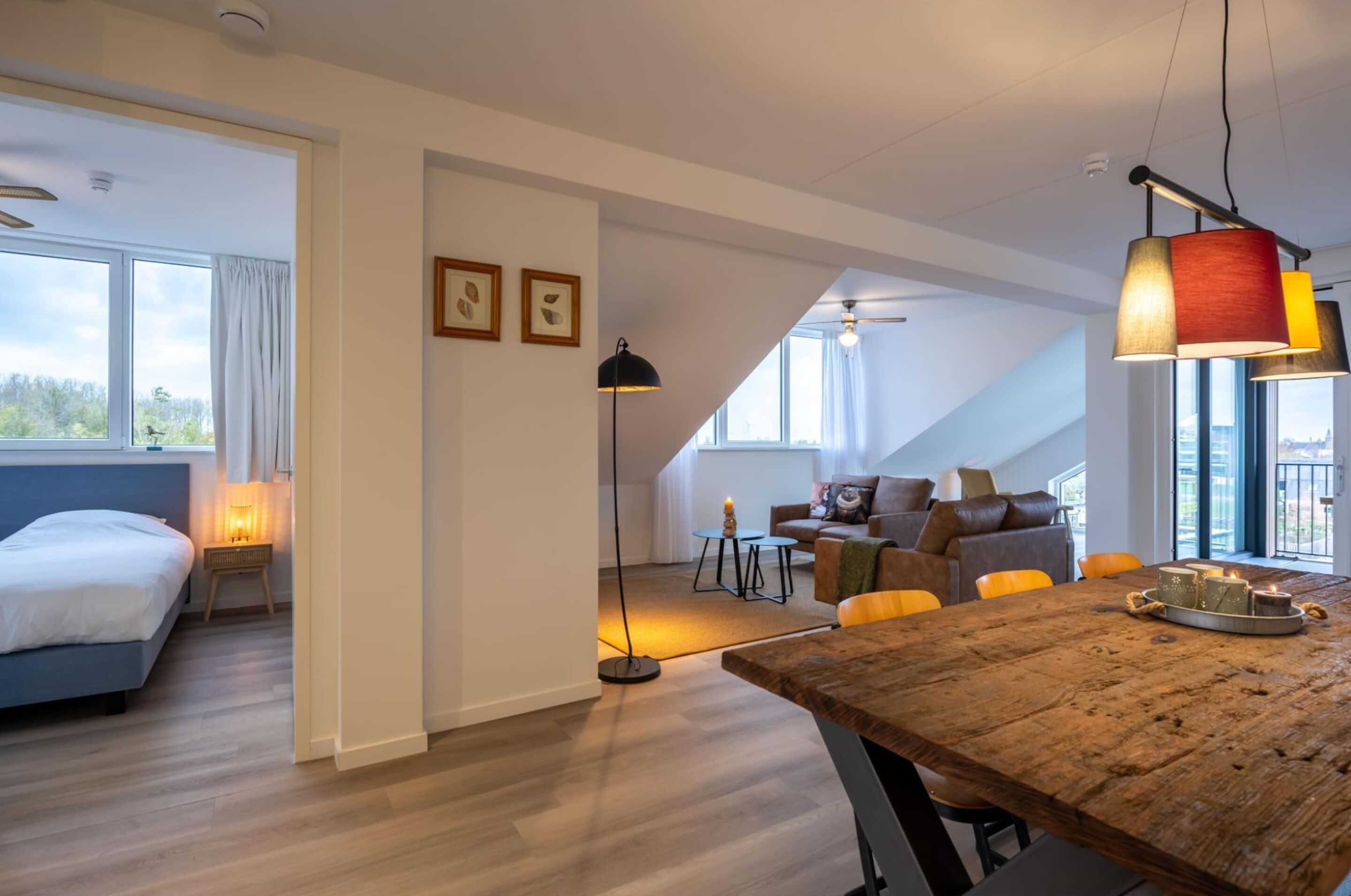 Een moderne, goed verlichte kamer met een houten eettafel, een bank en een bed.