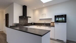 Una cocina moderna con una isla central, muebles blancos, una campana extractora negra y un horno empotrado.