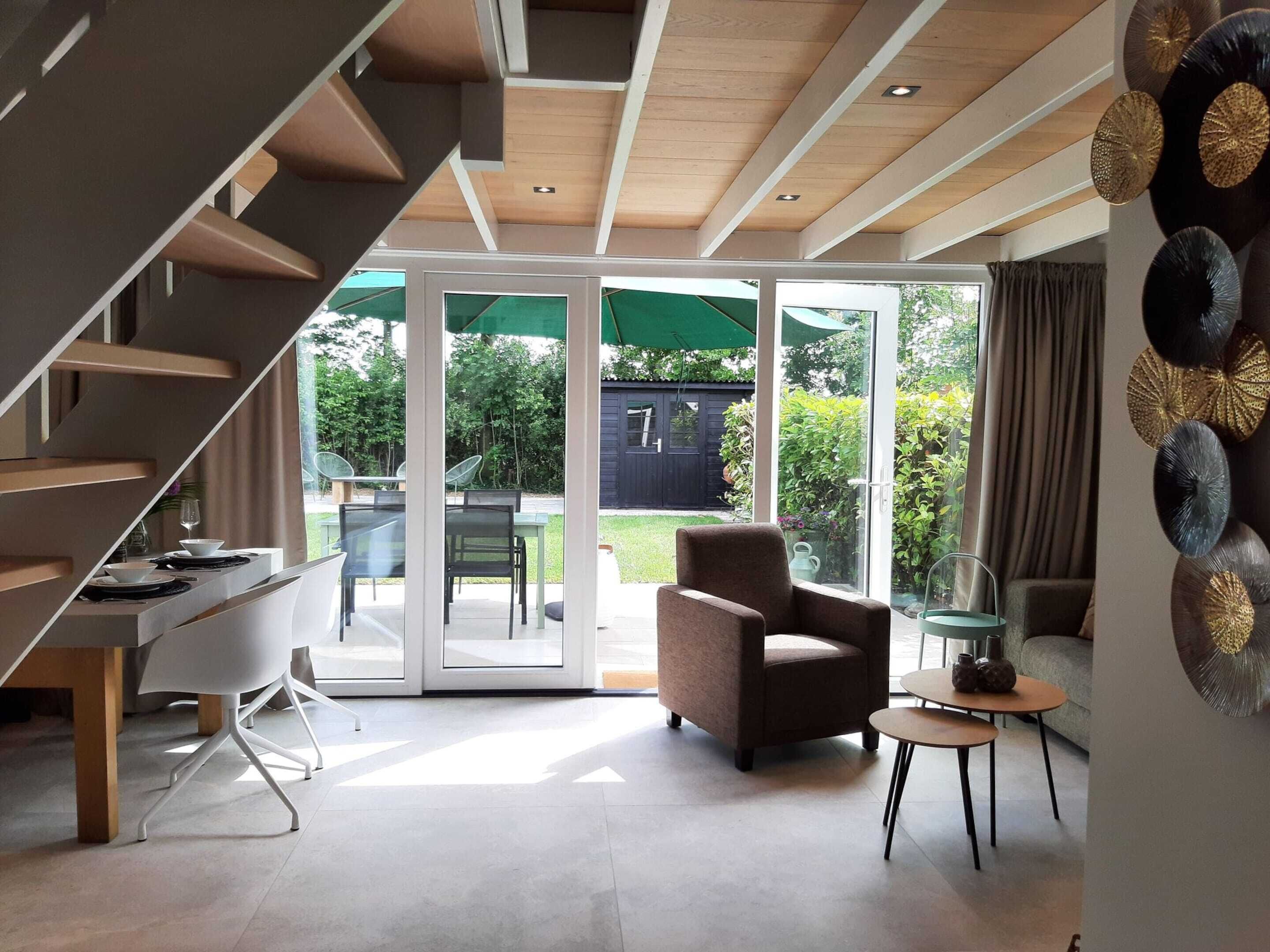 A modern interior with a staircase, a dining area, and a living space with a view of the outdoors.