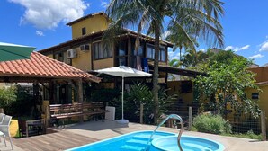 A swimming pool with a metal ladder, wooden deck, and a covered seating area with a bench and chairs. - Relax and enjoy recess time (RIO DE JANEIRO)