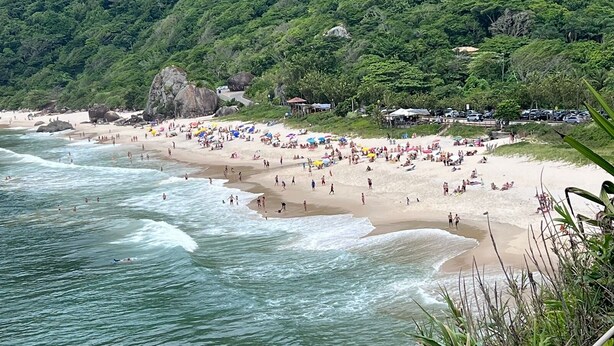 A beach with people and umbrellas, surrounded by lush green hills. - Relax and enjoy recess time (RIO DE JANEIRO)