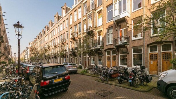 A row of traditional brick townhouses with balconies, parked cars, and bicycles along a cobblestone street. - Modern Apartment Overlooking the Harbor (The Hague)