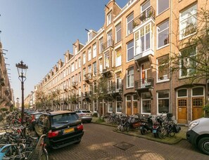 Una hilera de casas urbanas tradicionales de ladrillo con balcones, coches estacionados y bicicletas a lo largo de una calle adoquinada.