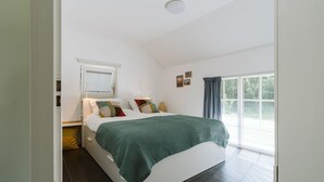A modern bedroom with a large bed, a window with blinds, a bedside table, and a ceiling light. - Luxurious 6-person Holiday Villa With a Forest Garden of 4000 m2 (Ouddorp)