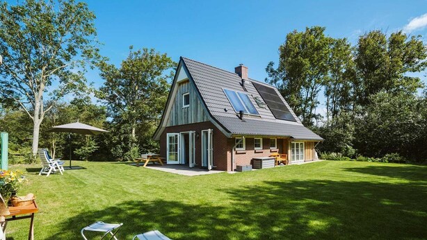 A two-story house with a sloped roof, large windows, and a well-maintained lawn. - Luxurious 6-person Holiday Villa With a Forest Garden of 4000 m2 (Ouddorp)