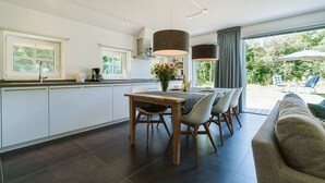 A modern kitchen with white cabinets, a dining table with chairs, and pendant lights. - Luxurious 6-person Holiday Villa With a Forest Garden of 4000 m2 (Ouddorp)