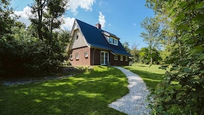 A house with a sloped roof, a gravel driveway, and a well-maintained lawn. - Luxurious 6-person Holiday Villa With a Forest Garden of 4000 m2 (Ouddorp)