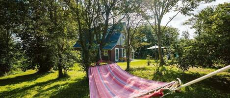 Una hamaca en un jardín verde exuberante, con una casa al fondo.